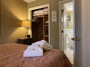 A neatly made bed with a patterned bedspread, a bedside lamp, a closet with hanging clothes, and a door leading to a bathroom. - Resort View - Ocean Villas C206-Professionally Managed by HHIB&T Vacation Rentals (Hilton Head Island)