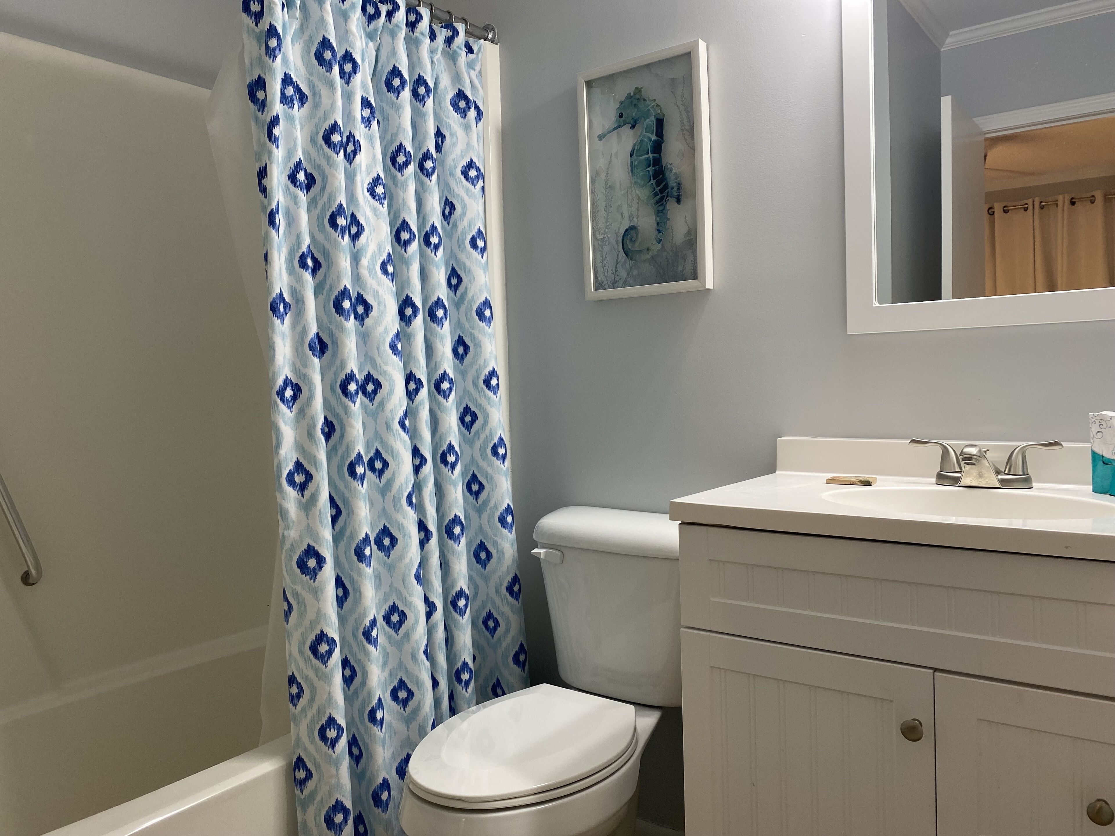 A bathroom with a shower curtain, toilet, sink, and cabinet.