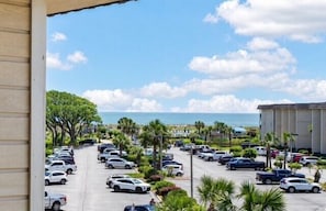 Un parking avec des voitures, des palmiers et une vue sur l’océan.