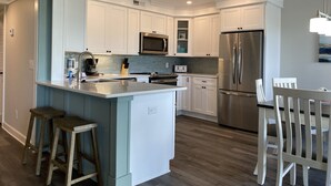 A modern kitchen with white cabinets, stainless steel appliances, and a central island with stools. - Ocean View - Admiral’s Row 110-Professionally Managed by HHIB&T Vacation Rentals (Hilton Head Island)
