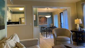Una sala de estar con un sofá color beige, un comedor con mesa y sillas, y una cocina visible a través de un pasillo abierto.