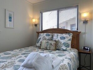 Een net opgemaakt bed met een beddekleed met dessin, twee kussens, een bedlampje en een wandklok.