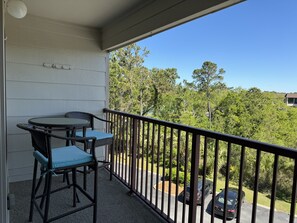 Un balcon avec une table et des chaises, une balustrade et une vue sur des arbres et un parking.
