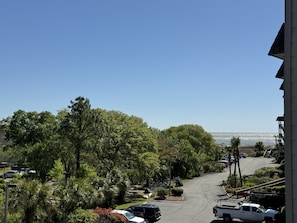 Rua residencial com carros estacionados, vegetação exuberante e vista clara para o oceano.