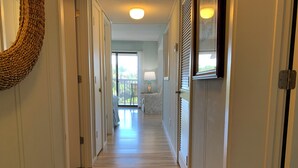 Ein Flur mit Holzboden, einer gewebten Wandtextil und Blick auf einen Balkon mit Bett und Lampe.