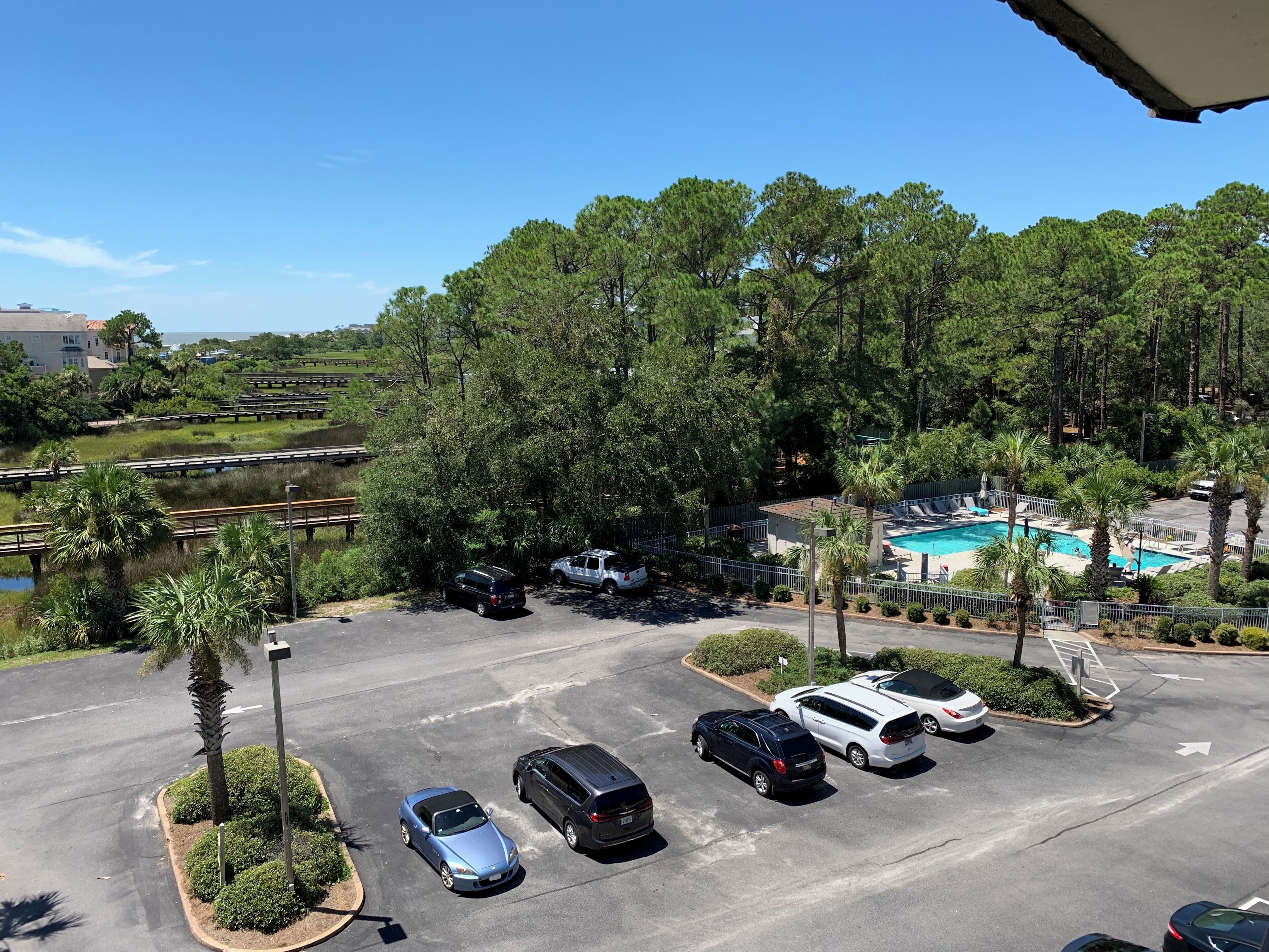 A parking lot with several cars, a swimming pool, and a view of a forested area.