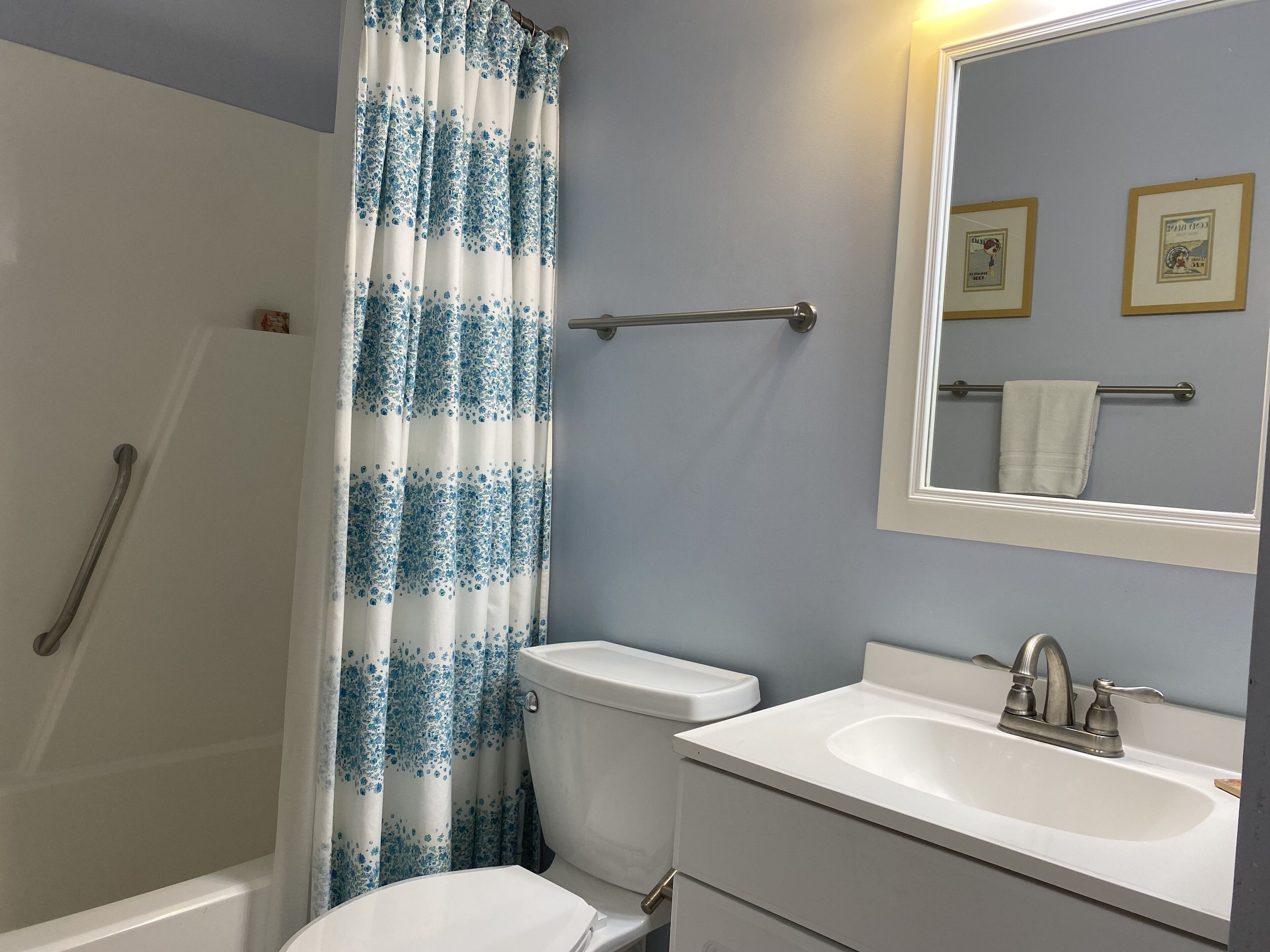 A bathroom with a shower curtain, toilet, sink, and a mirror with framed pictures.