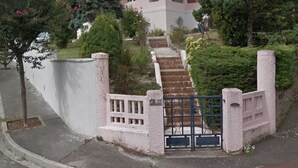 A two-story pink house with a front entrance, a small porch, and a staircase leading up to the door. - Town house near the ocean (20min) (Dax)