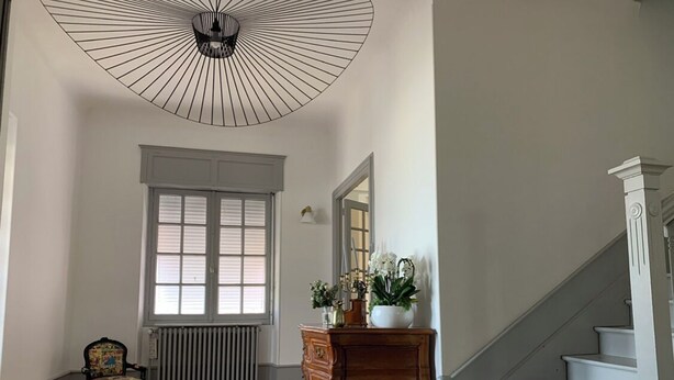 A spacious room with hardwood flooring, a radiator, a wooden dresser, a chair, a large window, and a staircase. - Town house near the ocean (20min) (Dax)