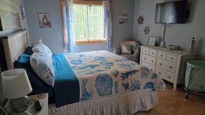 A bedroom with a bed, a dresser, a television, and a window with curtains.