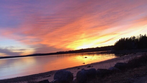A sunset over a calm lake with a rocky shoreline and a forest in the background.