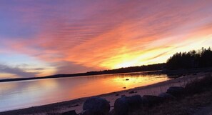 Ein Sonnenuntergang über einem stillen See mit felsigem Ufer und einem Wald im Hintergrund.