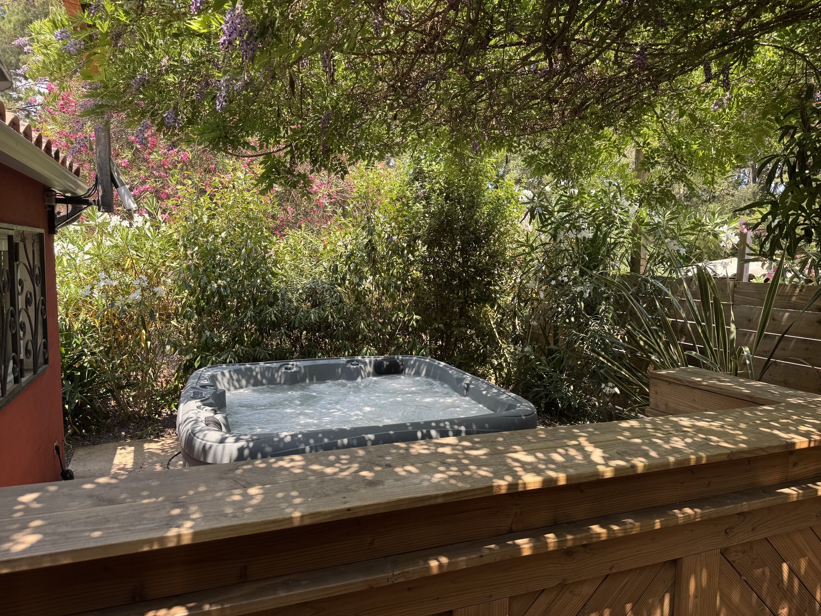 A hot tub in a garden with surrounding greenery and a wooden deck.