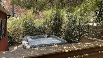 A hot tub in a garden with surrounding greenery and a wooden deck.