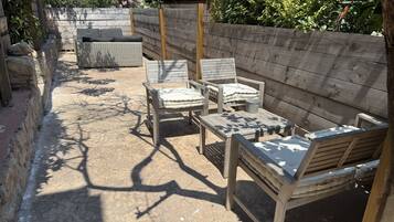 Un patio al aire libre con muebles de madera, incluyendo sillas y una mesa, rodeado por una cerca de madera y follaje.