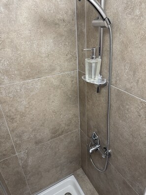 Ducha con cabezal de ducha de mano, dispensador de jabón de vidrio y grifo empotrado.