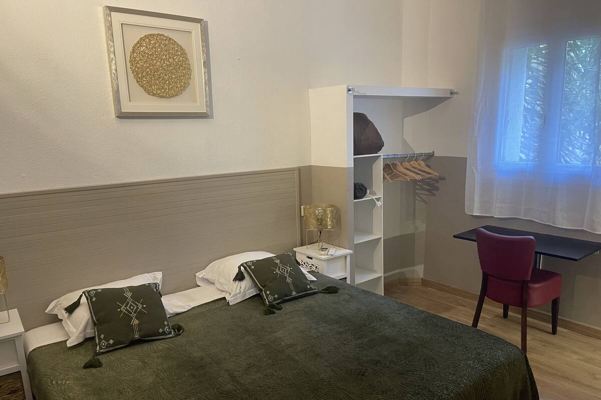 Un dormitorio ordenado con cama, mesitas de noche, un escritorio y una silla.
