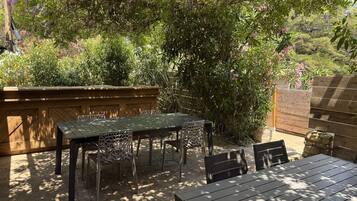 Un patio al aire libre con una mesa y sillas, rodeado de abundante follaje y una cerca de madera.