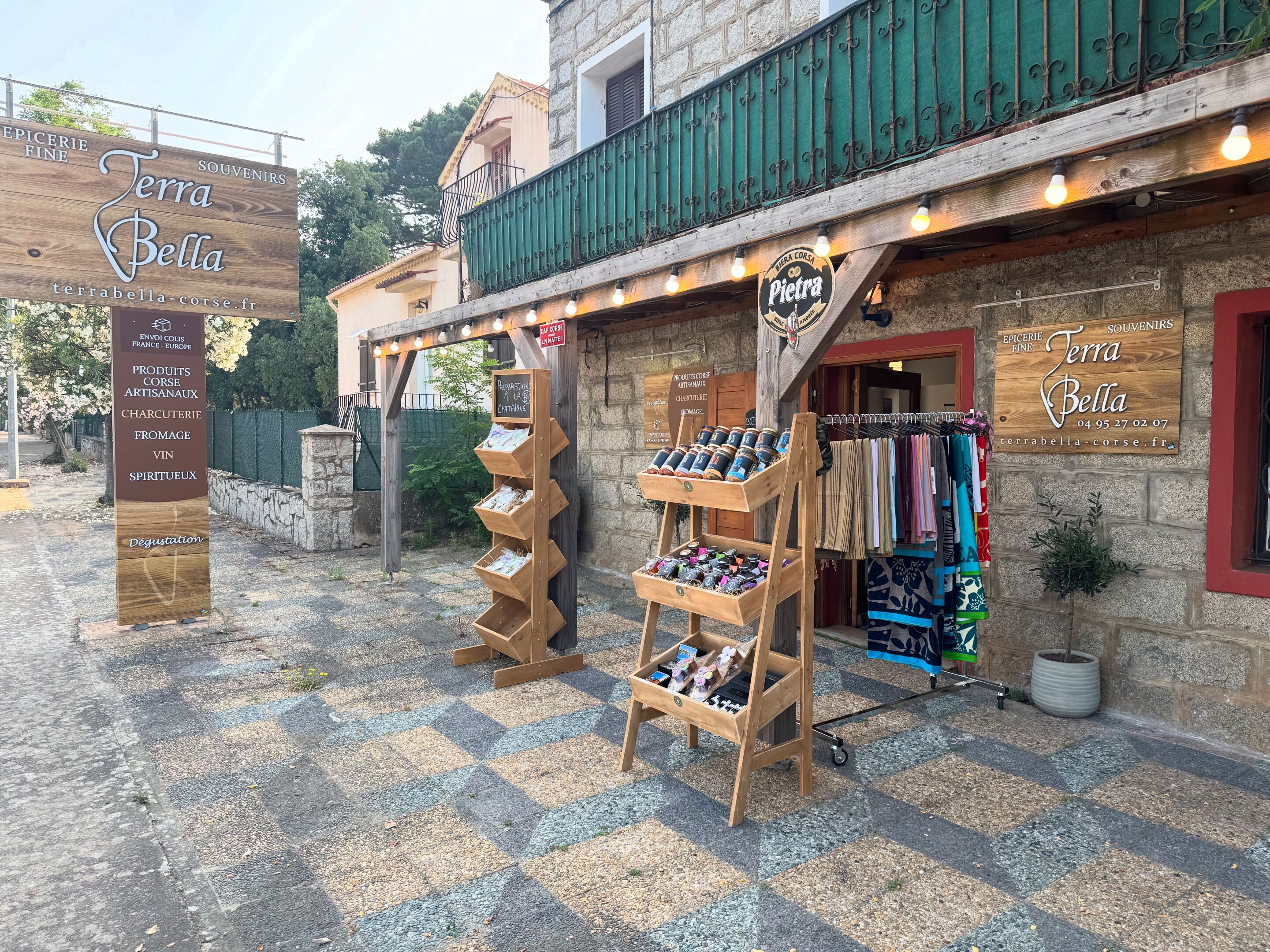 A storefront with a sign for Terra Bella, a wooden display stand with products, and a clothing rack outside.