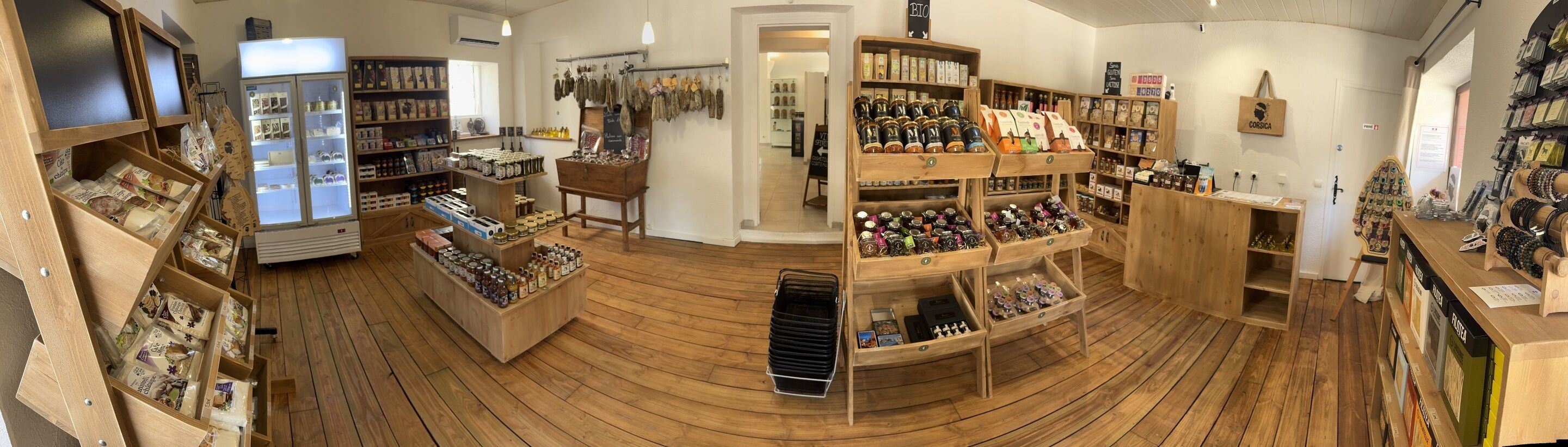 A store with wooden flooring, shelves with various products, and a refrigerator.