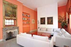 A living room with a fireplace, white sofas, a red coffee table, and bookshelves against an orange wall.
