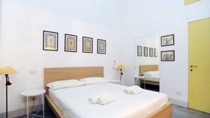Een moderne hotelkamer met een houten bed, wit beddengoed, een klein nachtkastje met een lamp en ingelijste foto's aan de muur.