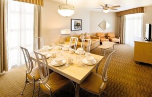 Une chambre d’hôtel comprenant un coin repas, un canapé, une télévision et un ventilateur de plafond.