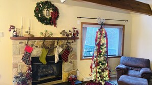 A cozy living room with a fireplace, a Christmas tree, and a comfortable armchair.