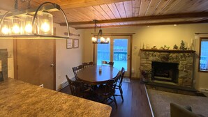 A dining area with a wooden table and chairs, a stone fireplace, and a view through a glass door to the outside.