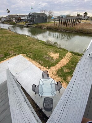 A view of a riverside deck with a glass table and chairs, surrounded by a wooden deck and a grassy area.