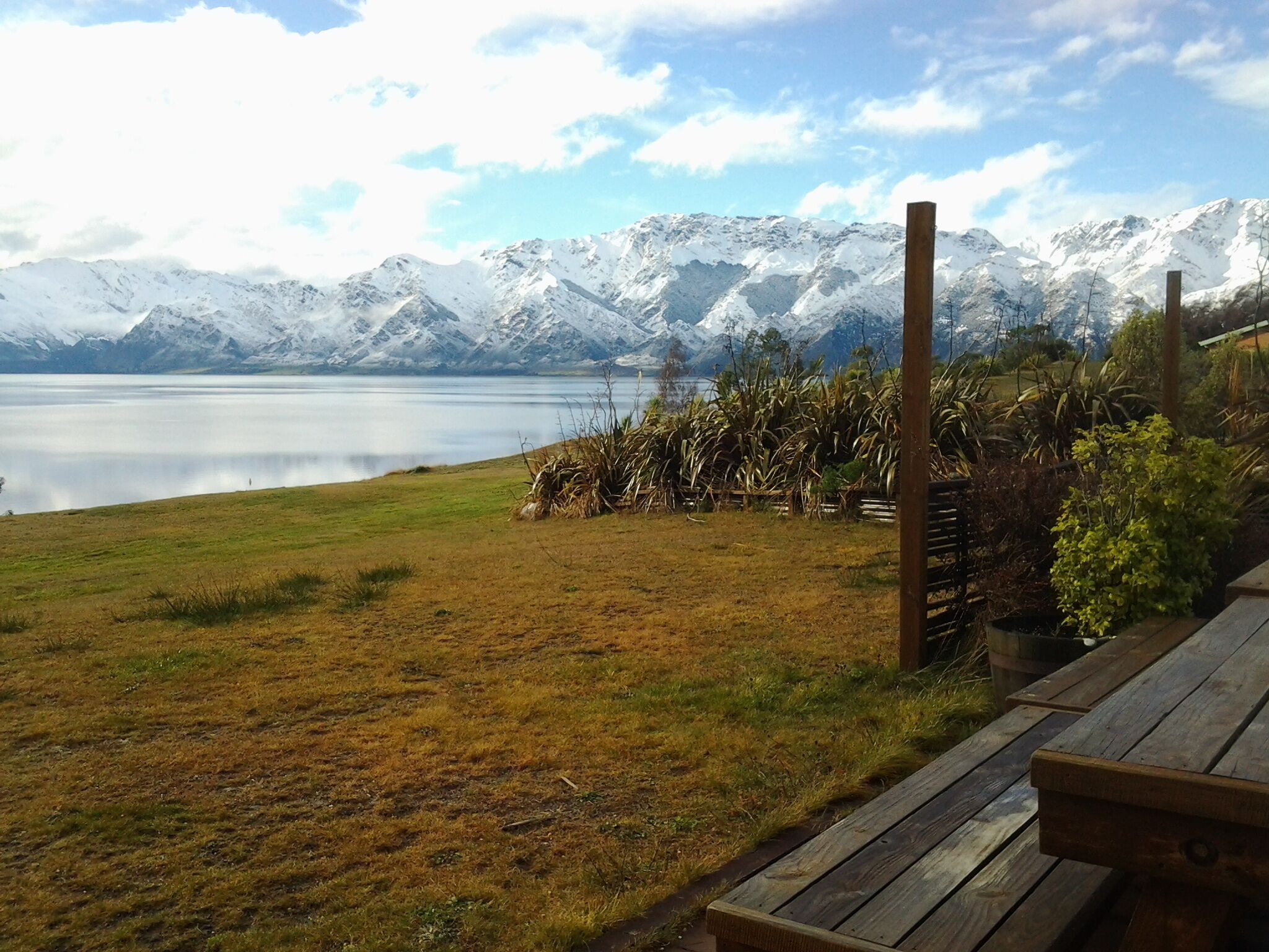 Vista sul lago con montagne sullo sfondo, una zona erbosa e un pontile in legno.