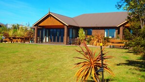 Eine Lodge mit einer großen Terrassenfläche, Gartenmöbeln im Freien und einem gepflegten Rasen.