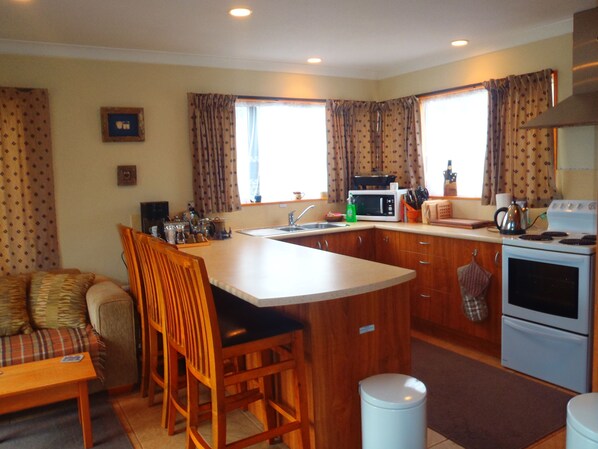 A compact kitchen with a central island, wooden chairs, a dining table, and a sofa.