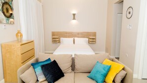 Une chambre à coucher avec un lit, une tête de lit en bois, une table de chevet et un canapé agrémenté de coussins colorés.