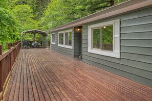 A deck with a dining area, a covered seating area, and a house with large windows. - Hot tub under the stars on the Washougal River! Close to Dougan Falls! (Washougal)
