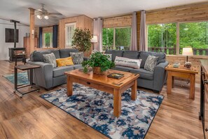 A cozy living room with a grey sofa, a wooden coffee table, and a large window with a view of greenery. - Hot tub under the stars on the Washougal River! Close to Dougan Falls! (Washougal)