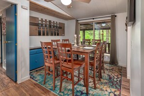 A dining area with a wooden table and chairs, a blue cabinet, and a large window with curtains. - Hot tub under the stars on the Washougal River! Close to Dougan Falls! (Washougal)