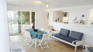 A modern living room with a round table, white sofa, and a sliding glass door leading to an outdoor area.