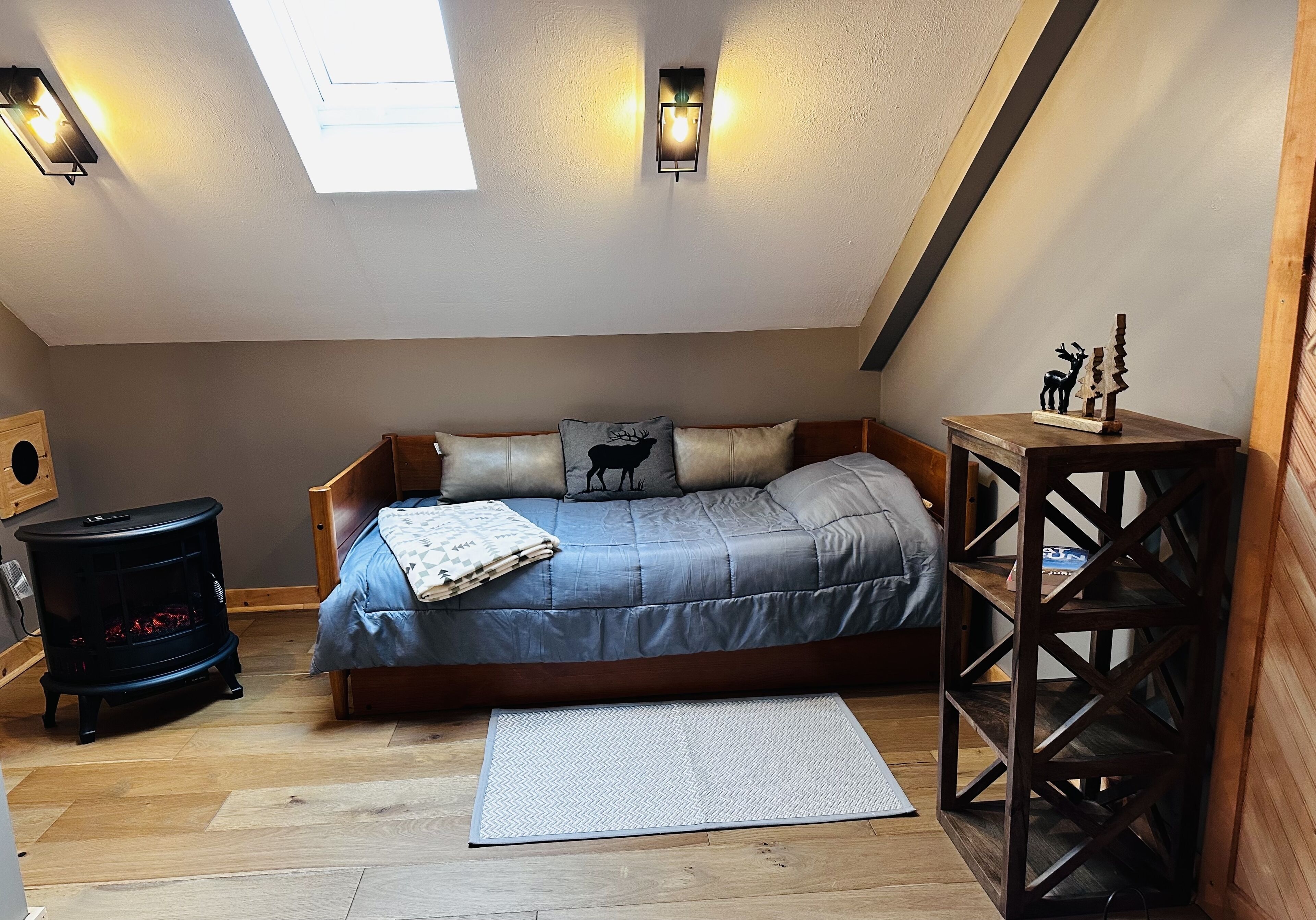 Un dormitorio acogedor en el ático con una cama, suelo de madera, un calentador pequeño y un tragaluz.