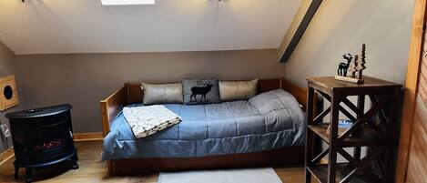 Un dormitorio acogedor en el ático con una cama, suelo de madera, un calentador pequeño y un tragaluz.