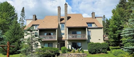 A two-story residential building with a stone facade, multiple chimneys, and a well-maintained lawn.