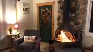 A cozy living room with a stone fireplace, a comfortable armchair, a small table with a lamp, and a door with decorative cutouts.