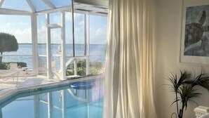 Une chambre dotée d’une grande fenêtre donnant sur une piscine et la mer.
