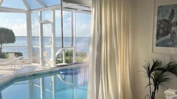 A room with a large window overlooking a pool and the sea. - Renovated Beach Cottage w/ Private Pool Steps Away from the Sea (North Side)