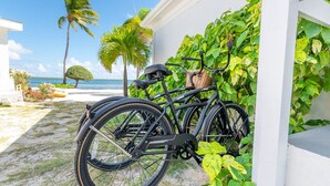 A bicycle parked against a white wall with a view of the beach and palm trees. - Renovated Beach Cottage w/ Private Pool Steps Away from the Sea (North Side)