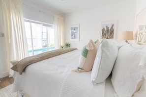 Ein Hotelzimmer mit einem großen Bett, Blick auf einen Swimmingpool und einen Strand.