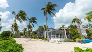 A beachside resort with palm trees, a glass building, and a sandy beach. - Renovated Beach Cottage w/ Private Pool Steps Away from the Sea (North Side)