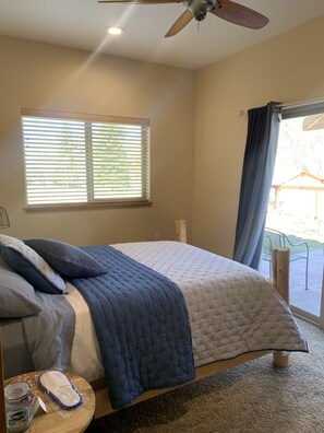 A bedroom with a bed, a ceiling fan, a window with blinds, and a view of the outside.