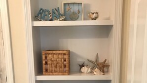 A storage unit with shelves holding folded towels, a wicker basket, and decorative items like starfish and a framed picture. - Walk to the Beach! (Middletown)