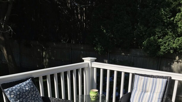 A deck with two wicker chairs, a small table, and a white railing. - Walk to the Beach! (Middletown)
